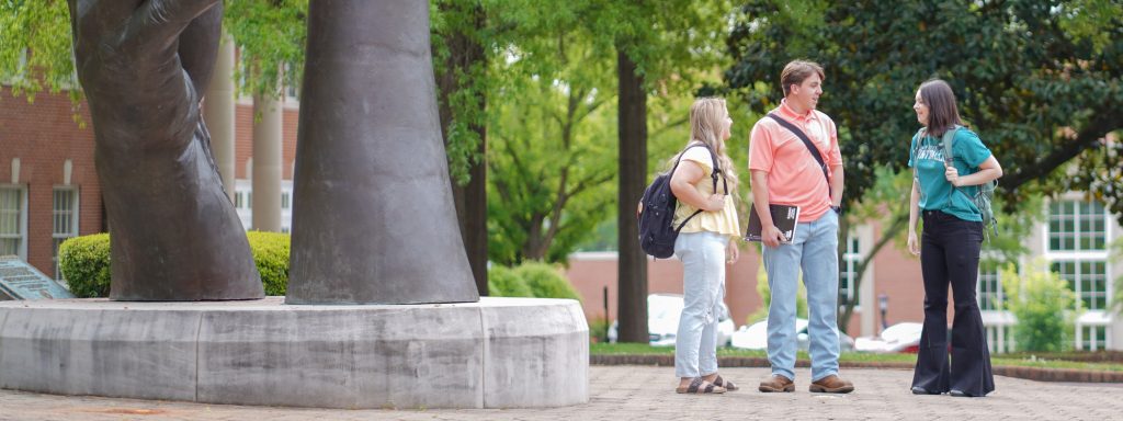 Three students converse next to The Becoming outdoor Landmark